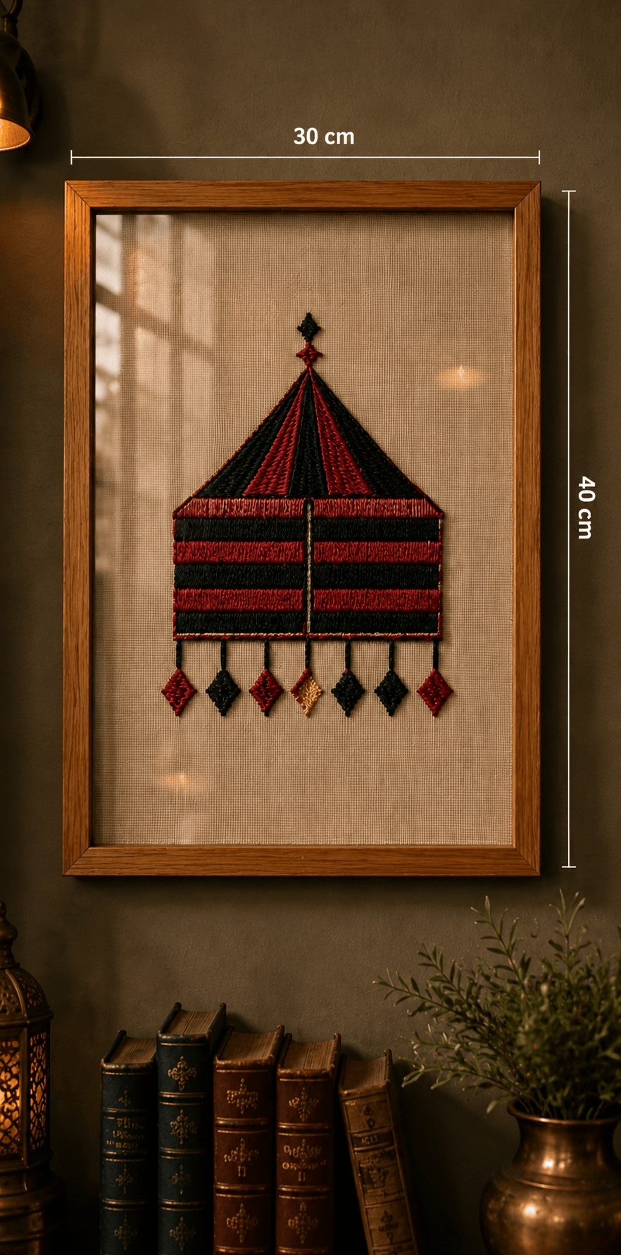 A framed decorative wall hanging or textile artwork featuring a stylized red and black tent-like motif on a beige background, shown in a wooden frame on a dark wall above books and a plant. White dimension lines indicate 30 cm width and 40 cm height.

